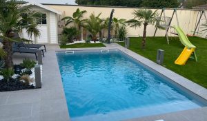 Piscine enterree dans une terrasse en carrelage dans un jardin