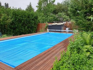 Couverture d'été de piscine à bulles bleue sur piscine enterrée avec terrasse en bois