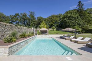 Piscine enterrée avec parasol, transats et végétation