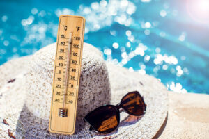 thermometre en bois posé au bord d'une piscine sur un chapeau a cote de lunettes de soleil