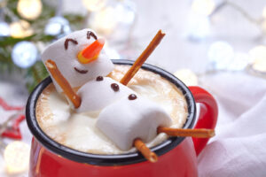 bonhomme de neige en guimauve qui flotte dans une tasse rouge de chocolat chaud au bord d'un sapin avec une guirlande