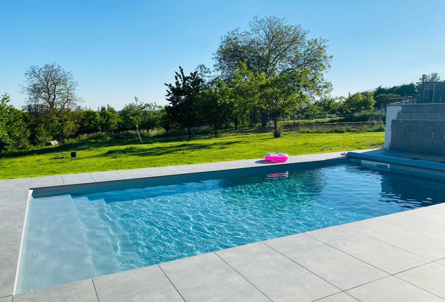 piscine enterree avec bouee rose dans un grand jardin